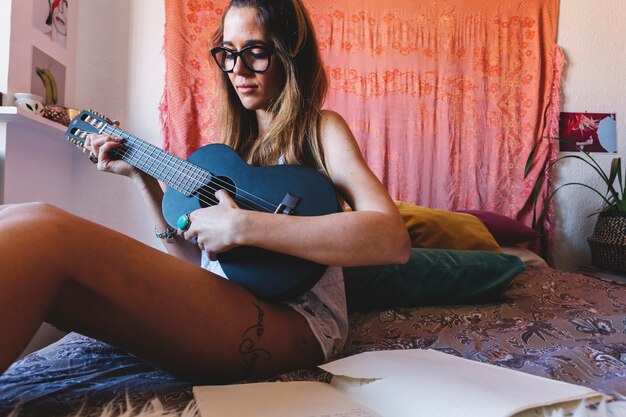 Женщина в очках, играющих гавайскую гитару на кровати