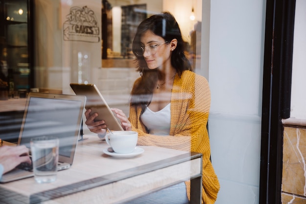 Foto gratuita donna in vetri facendo uso della compressa in caffè