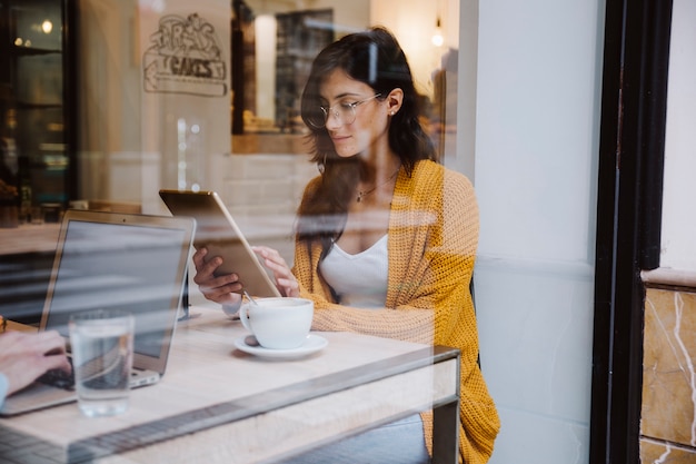 Free photo woman in glasses using tablet in cafe