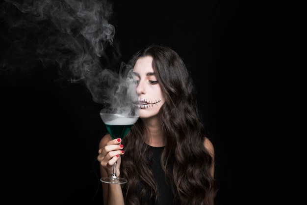 Woman goblet smelling at vapor of smoking turquoise liquid