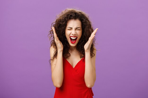 Woman going crazy screaming being tensed under pressure closing eyes shaking hands and yelling distressed and upset losing control over emotions posing displeased and fed up over purple background.