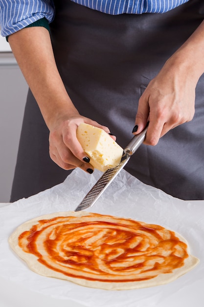 羊皮紙の上に自家製ピザのパンの上にチーズを格子の女性