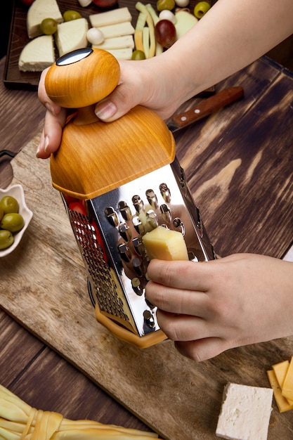 A woman grating cheese on a wood board with pickled olives side view
