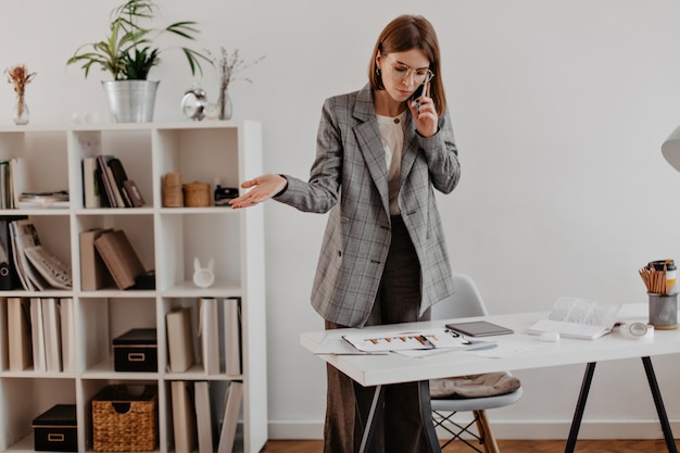 Free photo woman in gray suit talking on phone with business partners. portrait of adult lady looking at chart.