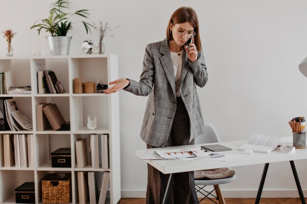 Woman in gray suit talking on phone with business partners. portrait of adult lady looking at chart.