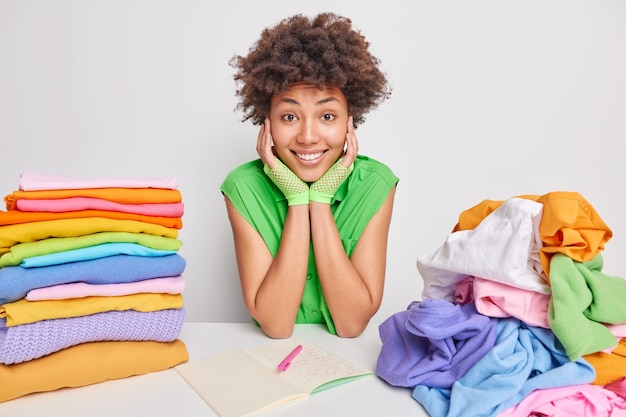 woman in green blouse sits at table folds clothes after washing and drying makes notes in notepad writes down list to do for weekends busy doing housework. Domestic chores