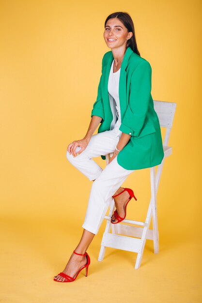 Woman in green jacket sitting on chair on yellow background