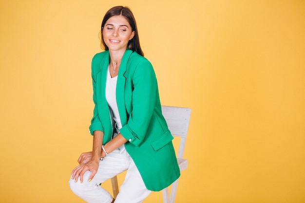 Woman in green jacket sitting on chair on yellow background