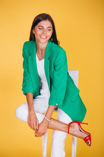 Woman in green jacket sitting on chair on yellow background