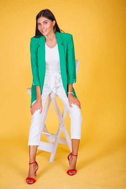 Woman in green jacket sitting on chair on yellow background