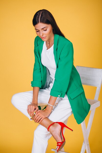 Woman in green jacket sitting on chair on yellow background