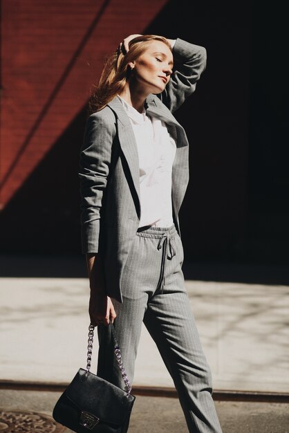 Woman in grey suit poses with black bag on the street of New York