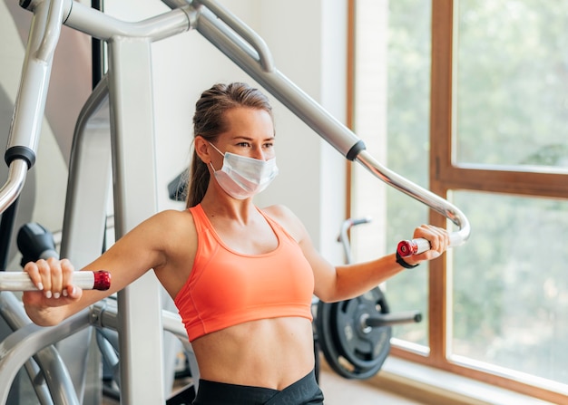 Женщина в тренажерном зале делает упражнения с медицинской маской