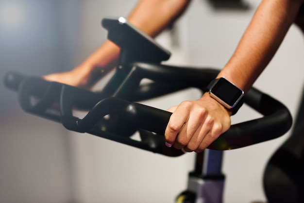 Woman at a gym doing spinning or cyclo indoor with smart watch