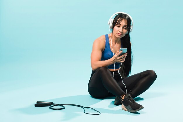 Женщина в спортивном наряде слушает музыку в наушниках со скакалкой