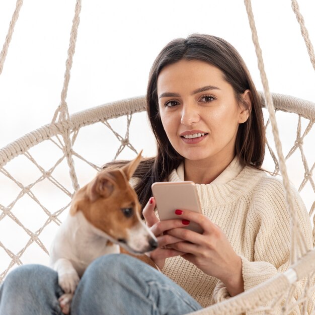 彼女の犬とスマートフォンでハンモックの女性