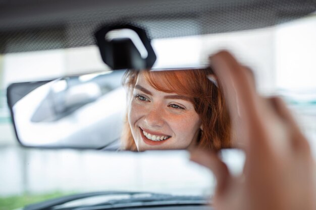 Woman hand adjusting rear view mirror of her car Happy young woman driver looking adjusting rear view car mirror making sure line is free visibility is good