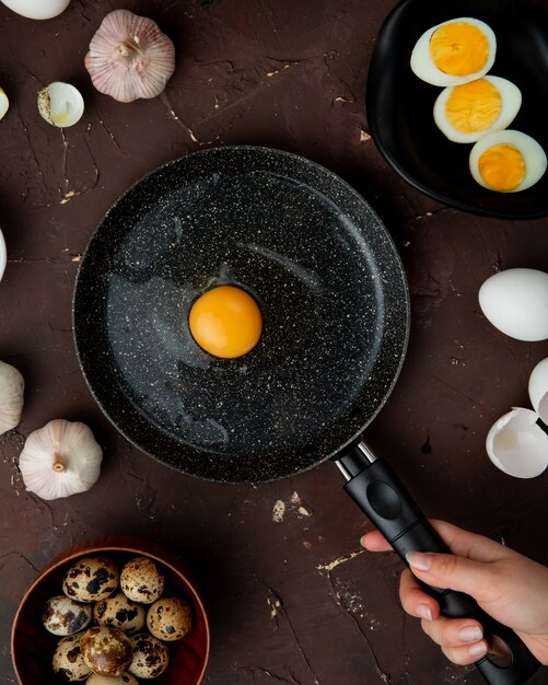  woman hand cooking egg with garlic eggs around on maroon table