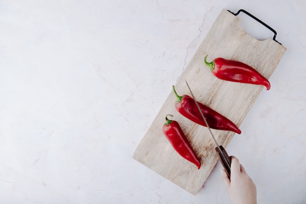  woman hand cutting pepper on cutting board with knife on right side and white table with copy space