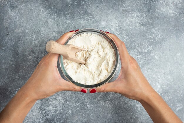 Woman hand holding bowl of flour on marble.