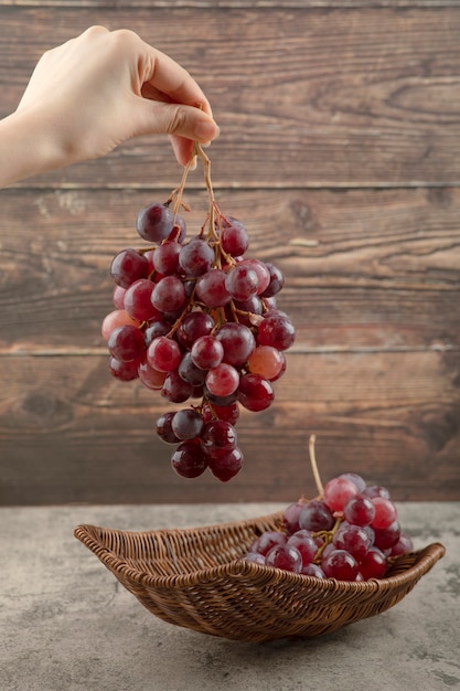 Женщина рука гроздь красного винограда на деревянных фоне.
