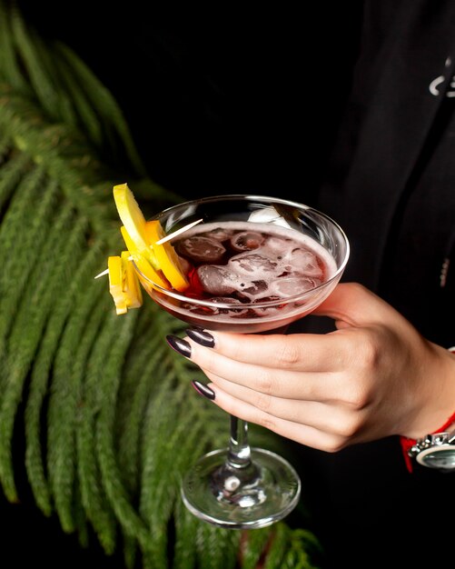 Woman hand holding a cocktail glass with fruit pieces on bamboo skewer