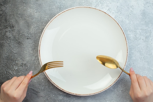 Женщина рука набор столовых приборов на пустой тарелке на серой поверхности