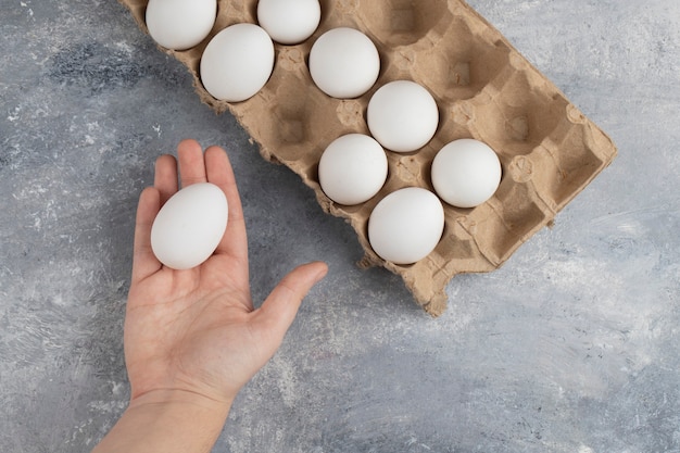 Mano della donna che tiene un uovo di gallina bianco fresco su un marmo.