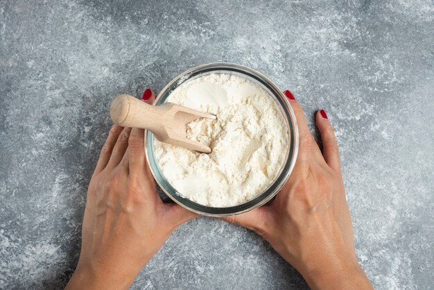 Woman hand holding glass bowl of flour on marble.