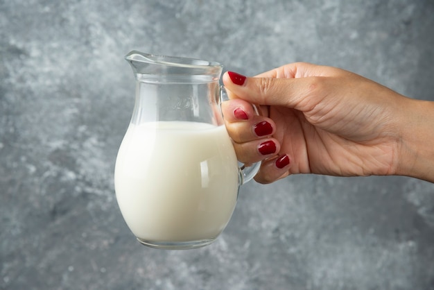 Mano della donna che tiene un vasetto di vetro di latte su marmo.