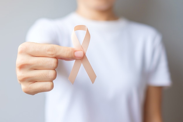 Woman hand holding peach ribbon for september uterine cancer awareness month. healthcare and world cancer day concept