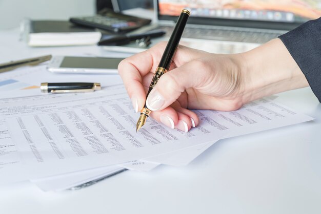 Woman hand holding pen at desk with papers