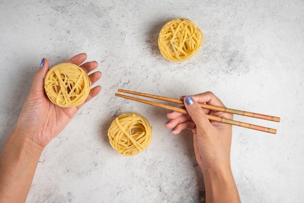 흰색 표면에 나무 젓가락으로 원시 tagliatelle 파스타를 들고 여자 손.