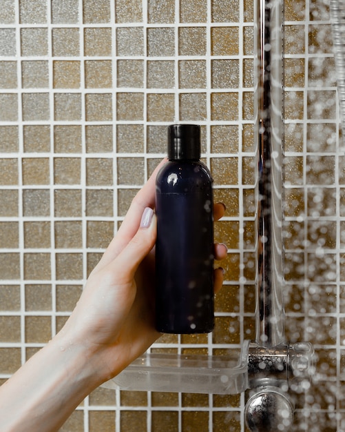 Woman hand holding shower gel in navy bottle in the bathroom