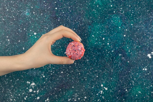 Woman hand holding a small pink doughnut .