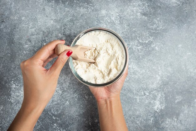 Woman hand holding spoon inside of flour bowl.