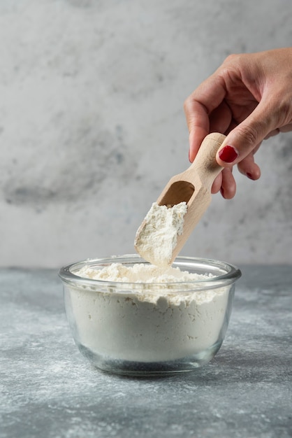 Woman hand holding spoon on top of flour bowl.
