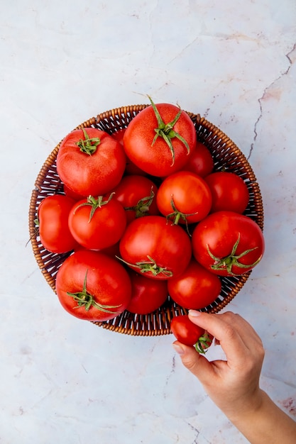 Woman hand holding tomato and basket of tomatoes on white surface