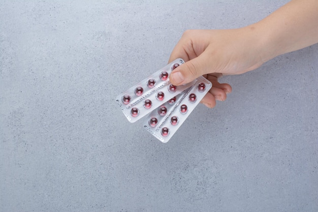 Woman hand holding two packs of pills on marble.