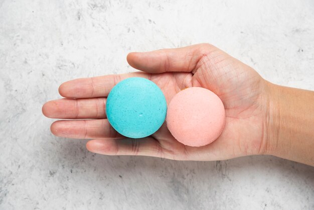 Woman hand holding two tasty macarons on marble surface.