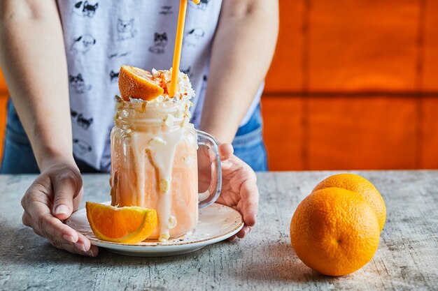 A woman hand holding a white plate with orange smoothie and slice of orange 