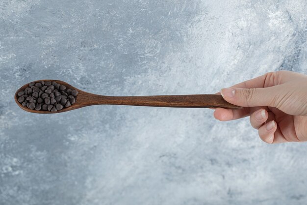 チョコレートチップの木のスプーンを持っている女性の手。