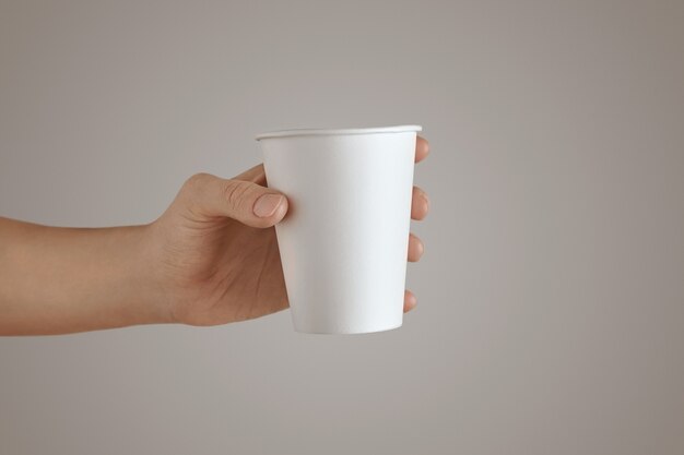 Woman hand holds blank empty take away paper glass side view, Isolated, unrecognizable