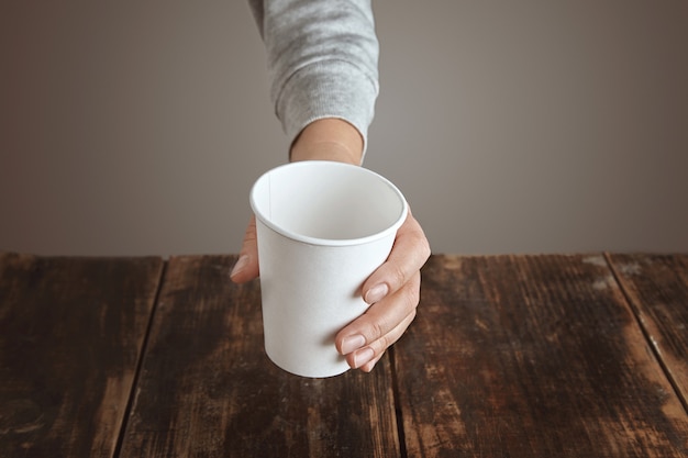 La mano della donna tiene la vista superiore di vetro di carta vuota vuota in bianco, sopra il tavolo in legno spazzolato invecchiato vintage. isolato, irriconoscibile