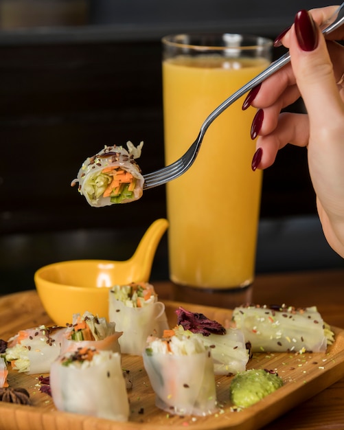 Woman hand holds in fork spring rolls with cucumber, carrot and lettuce