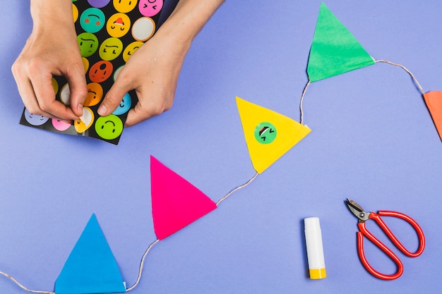 Woman hand making bunting with emoji stickers over colored background