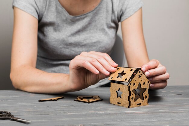 Рука женщины делая творческий небольшой дом на деревянном столе