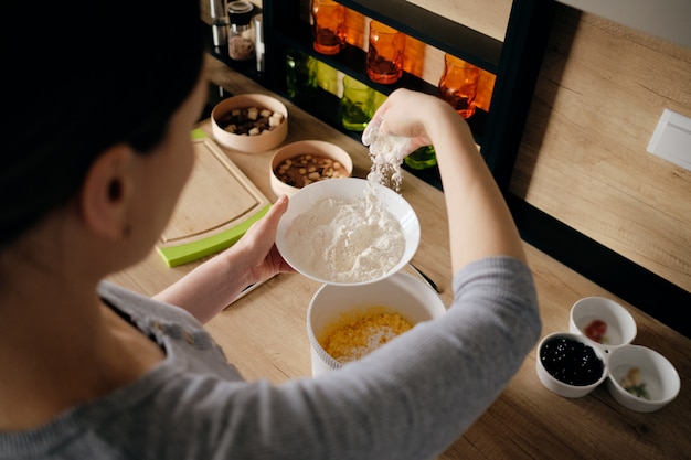 Free photo woman hand sprinkling flour in a white bowl