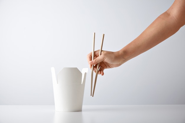 Woman hand with chopsticks near blank takeway box with tasty noodles isolated on white Retail set presentation