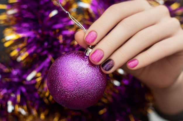 クリスマスと新年のネイルデザインの女性の手はきらびやかなおもちゃの球体を保持します。